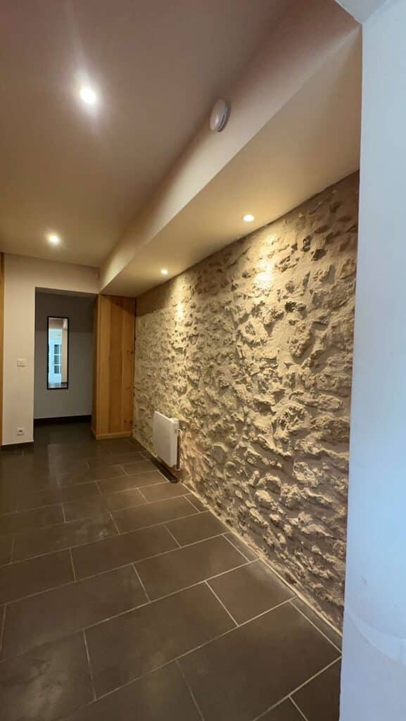 Intérieur avec Mur Pierre Apparente et Sol Ardoise Hall d'entrée rénové avec mur en pierres apparentes texturé, éclairage encastré chaud, chauffage mural et sol en grandes dalles sombres.